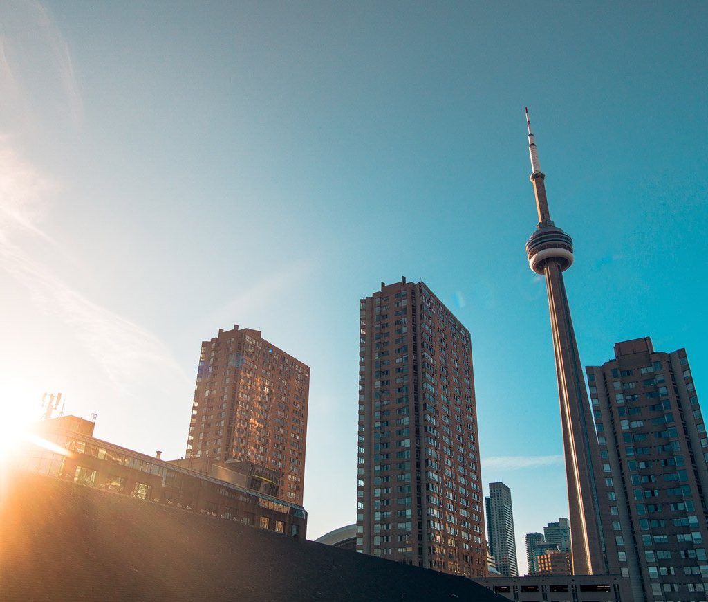 The CN Tower sits in between 2 tall brown buildings to the left and one tall brown building to the right.